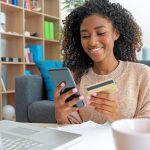Cheerful young black woman using her credit union credit card at home