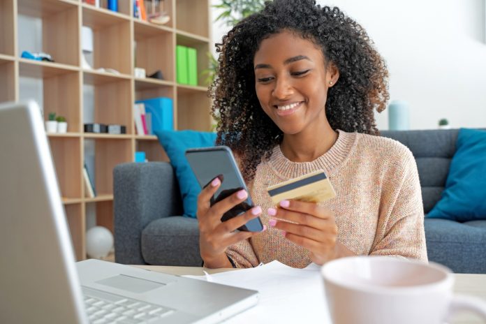 Cheerful young black woman using her credit union credit card at home