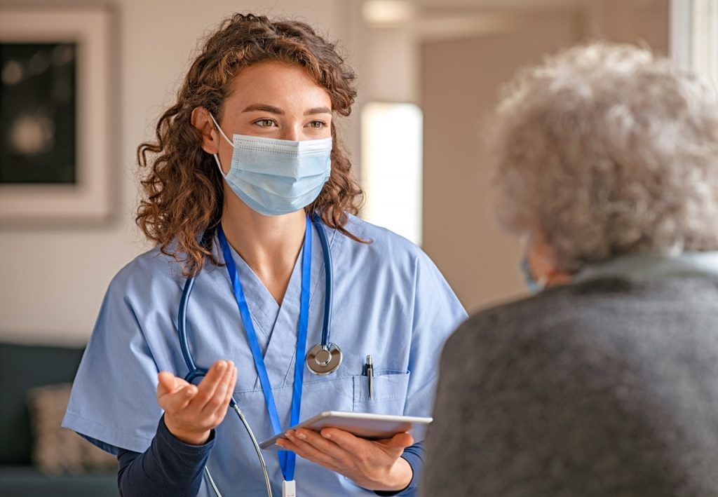 Barriers to healthcare interoperability and how to overcome them - Young doctor visits senior woman with surgical mask