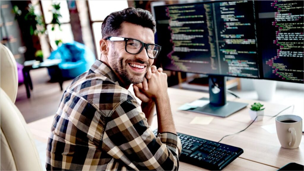 A web developer smiles in front of a monitor with lines of code