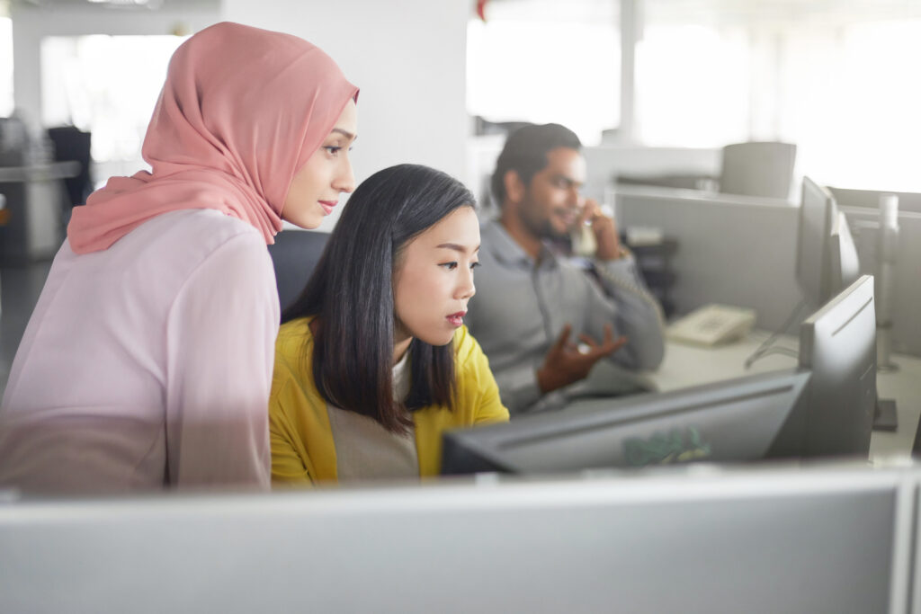 Businesswomen discussing over desktop PC in office. Female colleagues are looking in computer monitor. They are at workplace.