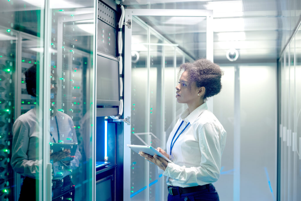 Medium shot of female technician working on a tablet in a data center full of rack servers running diagnostics and maintenance on the system