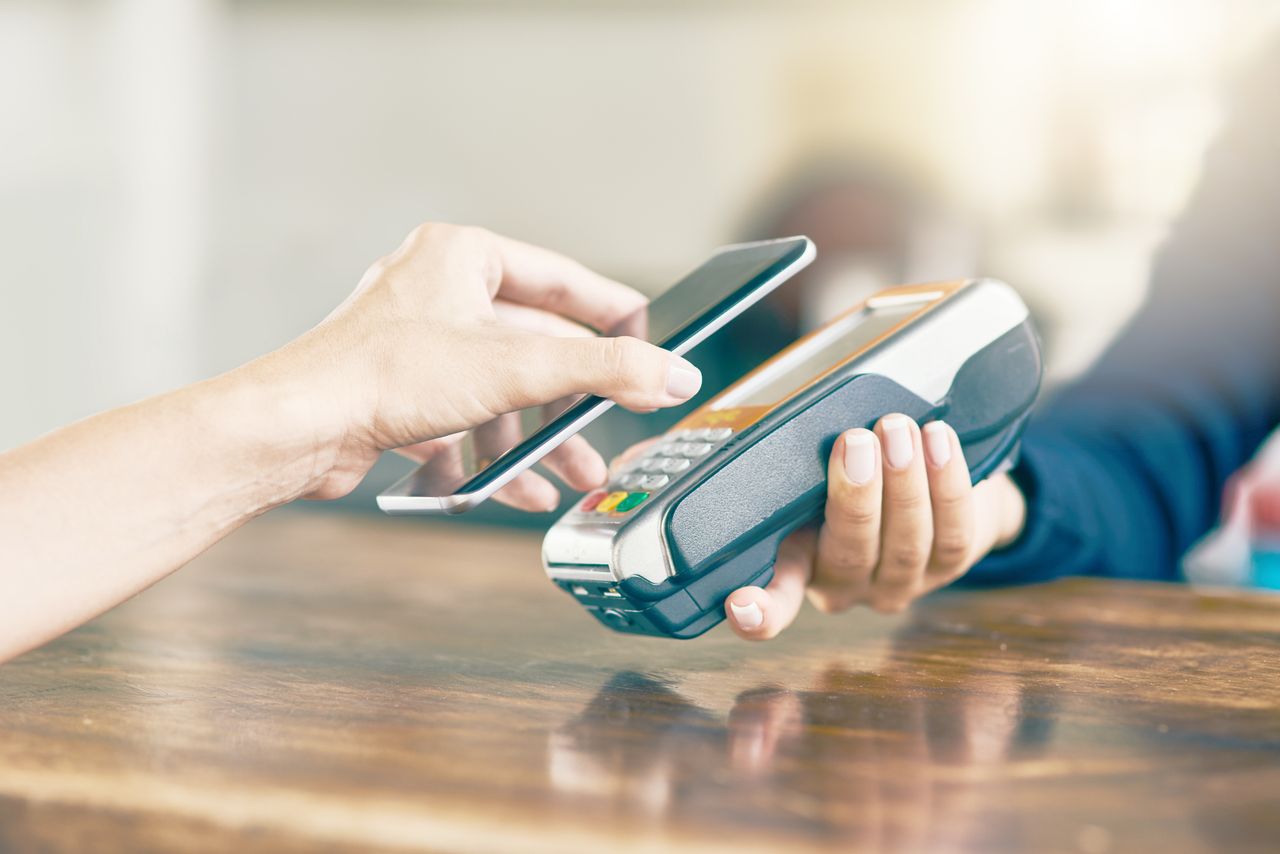 Closeup of an unrecognizable person using her phone to scan and pay a bill on a card machine at a cafe during the day