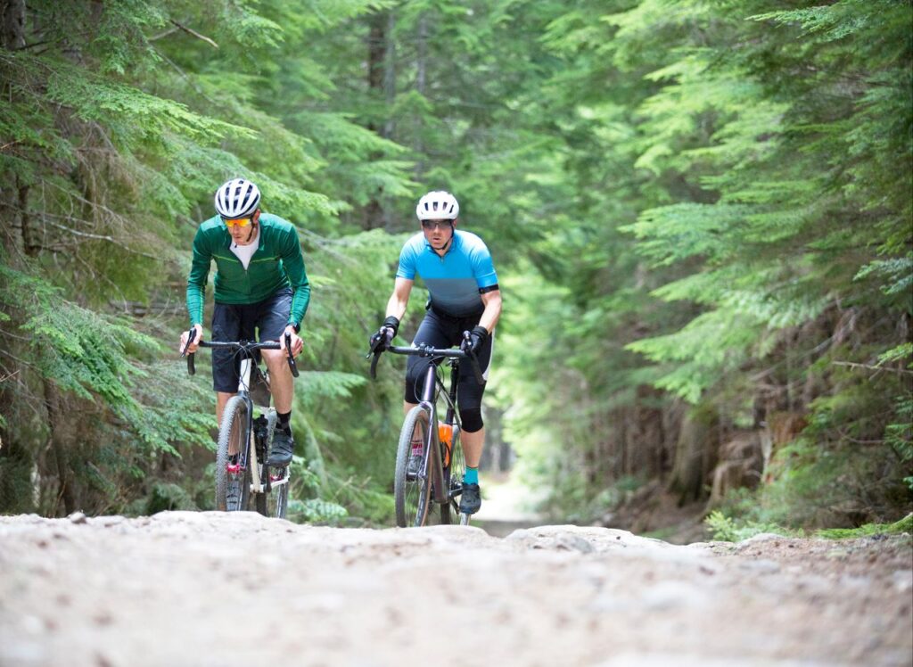 Two men go for a backcountry bicycle ride with their gravel road bikes on a forestry road. Their bikes are similar to cyclo-cross bikes with disc brakes and oversized tires suited for the rough terrain.