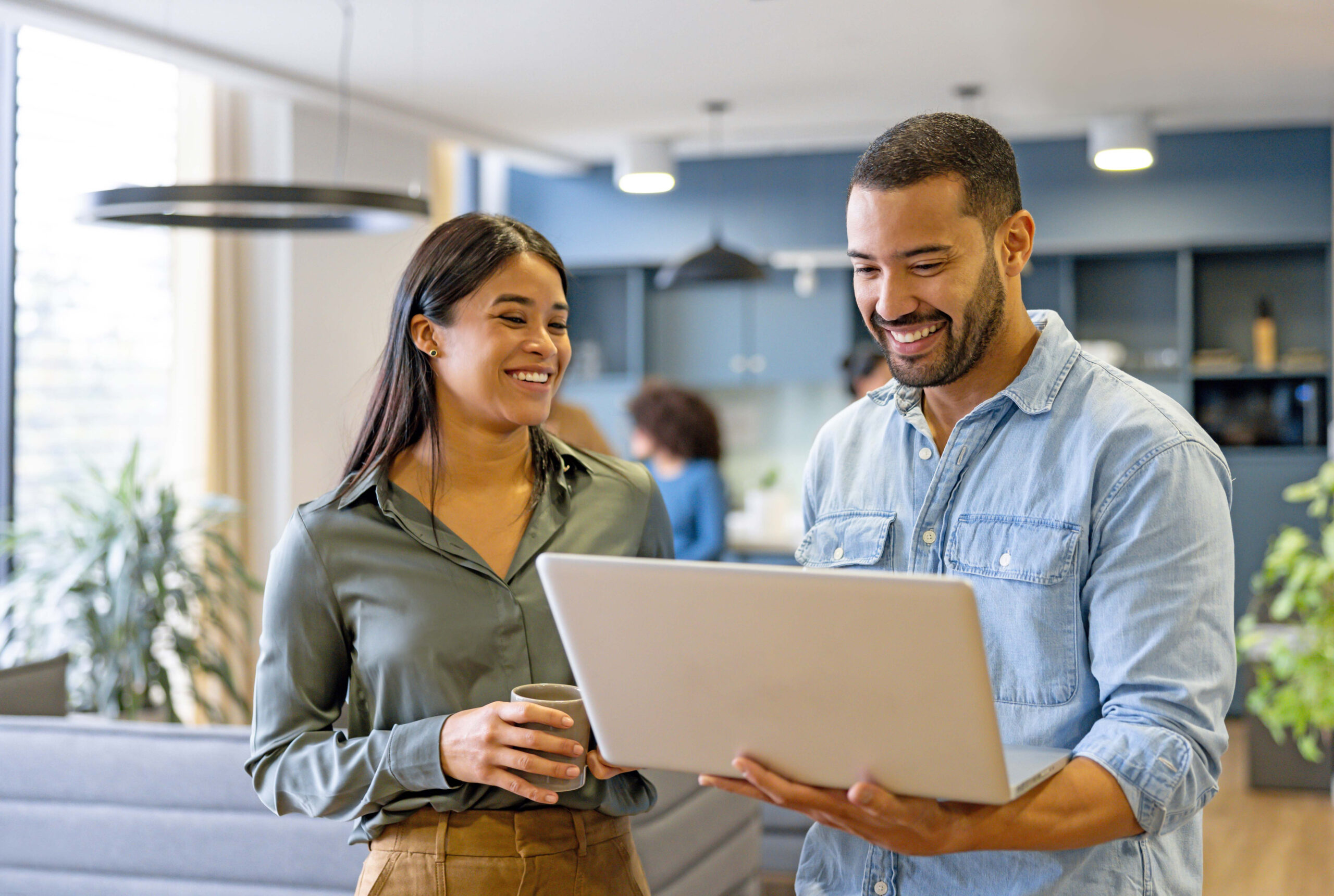 A man and a woman in an office, a man is holding a white laptop