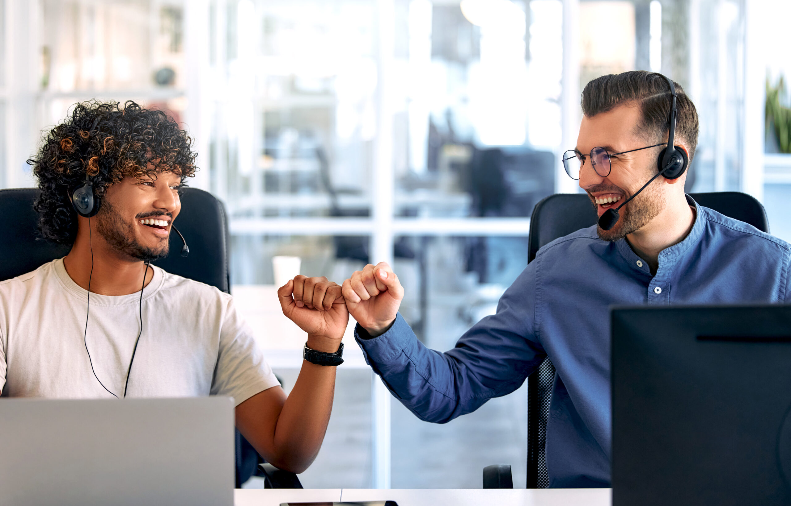 Call center employee accompanied by his team. Focused support operator at work. Young employee working with headset and laptop.