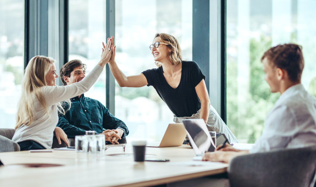 Profissional do sexo feminino dando um high five a sua colega na sala de reuniões. Grupo de colegas comemorando o sucesso em uma reunião.