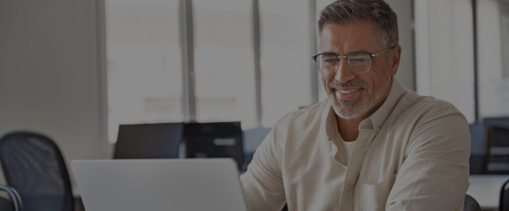 man wearing glasses using the computer and smiling