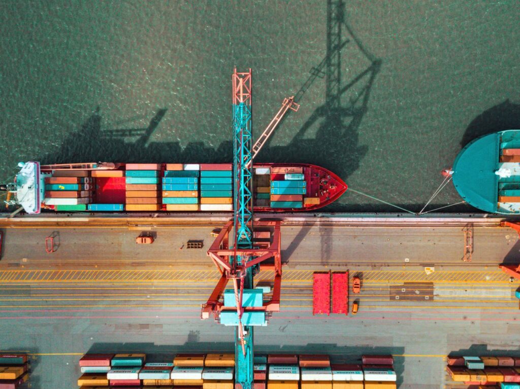 Top-down view of a container ship being loaded at a port with cranes and stacked containers, illustrating complex B2B integration workflows and global data exchange enhanced by AI.