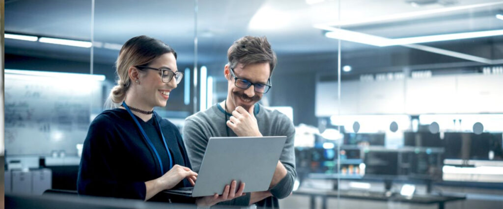 Woman smiling in an office, showing something to a man, also smiling, on her laptop